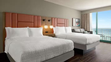 A hotel room with two beds, a nightstand, a desk, and a view of the ocean.