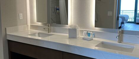 A modern bathroom with two sinks, a large mirror, and a shower area.