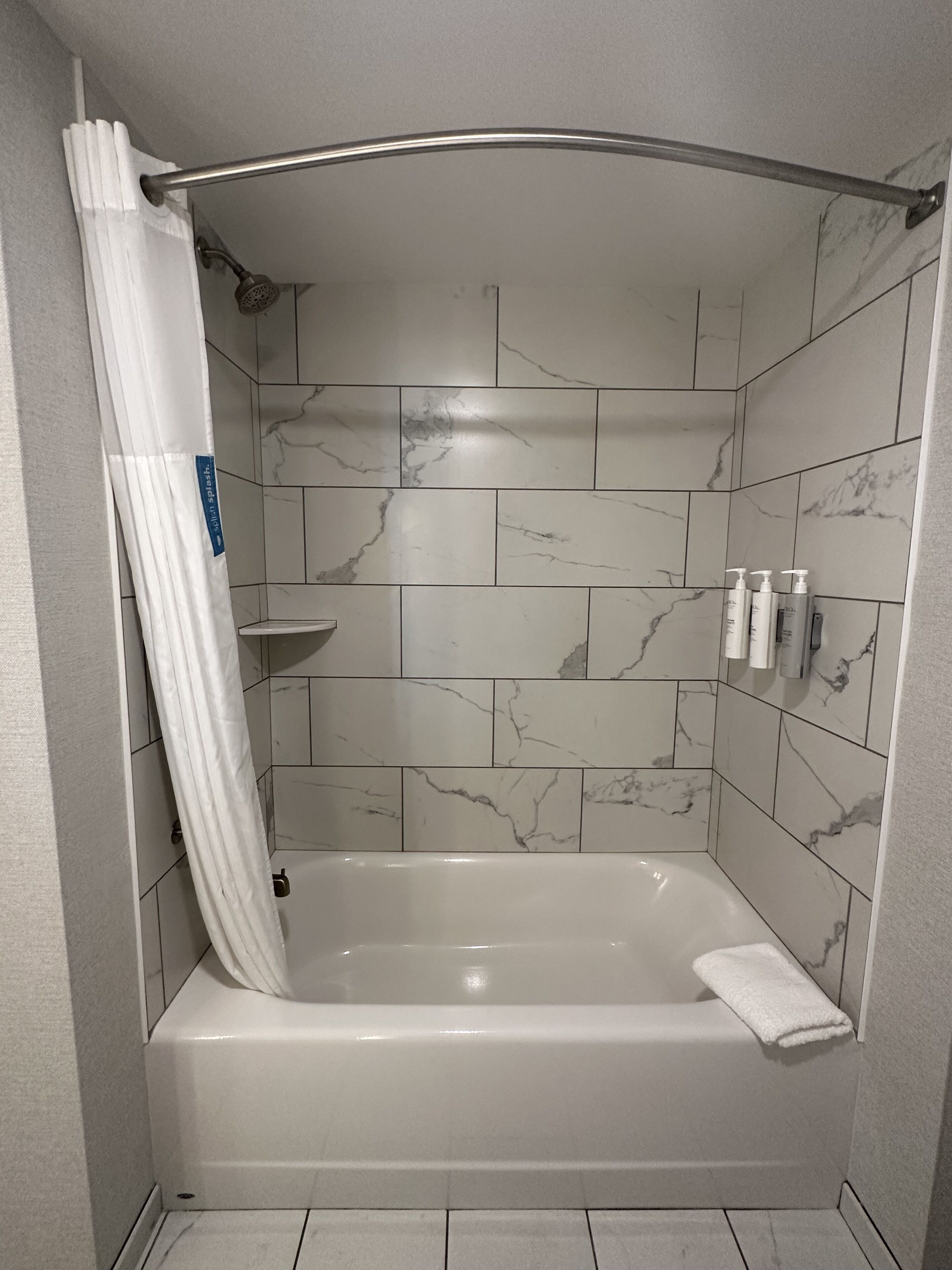 Un baño moderno con una bañera independiente, azulejos de mármol, una cortina de ducha y artículos de aseo en la pared.