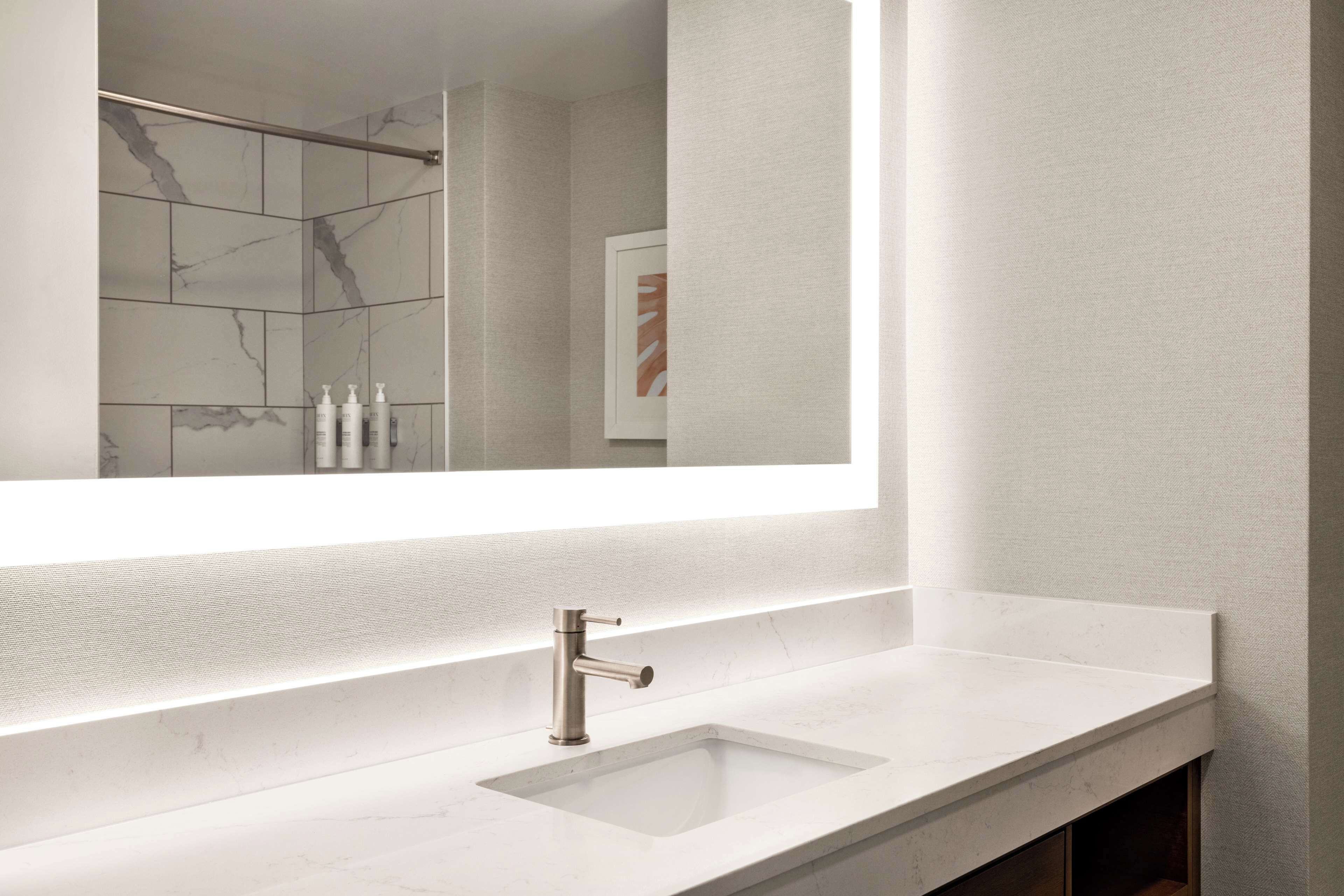 A modern bathroom with a large mirror, a white sink, and a shower area.