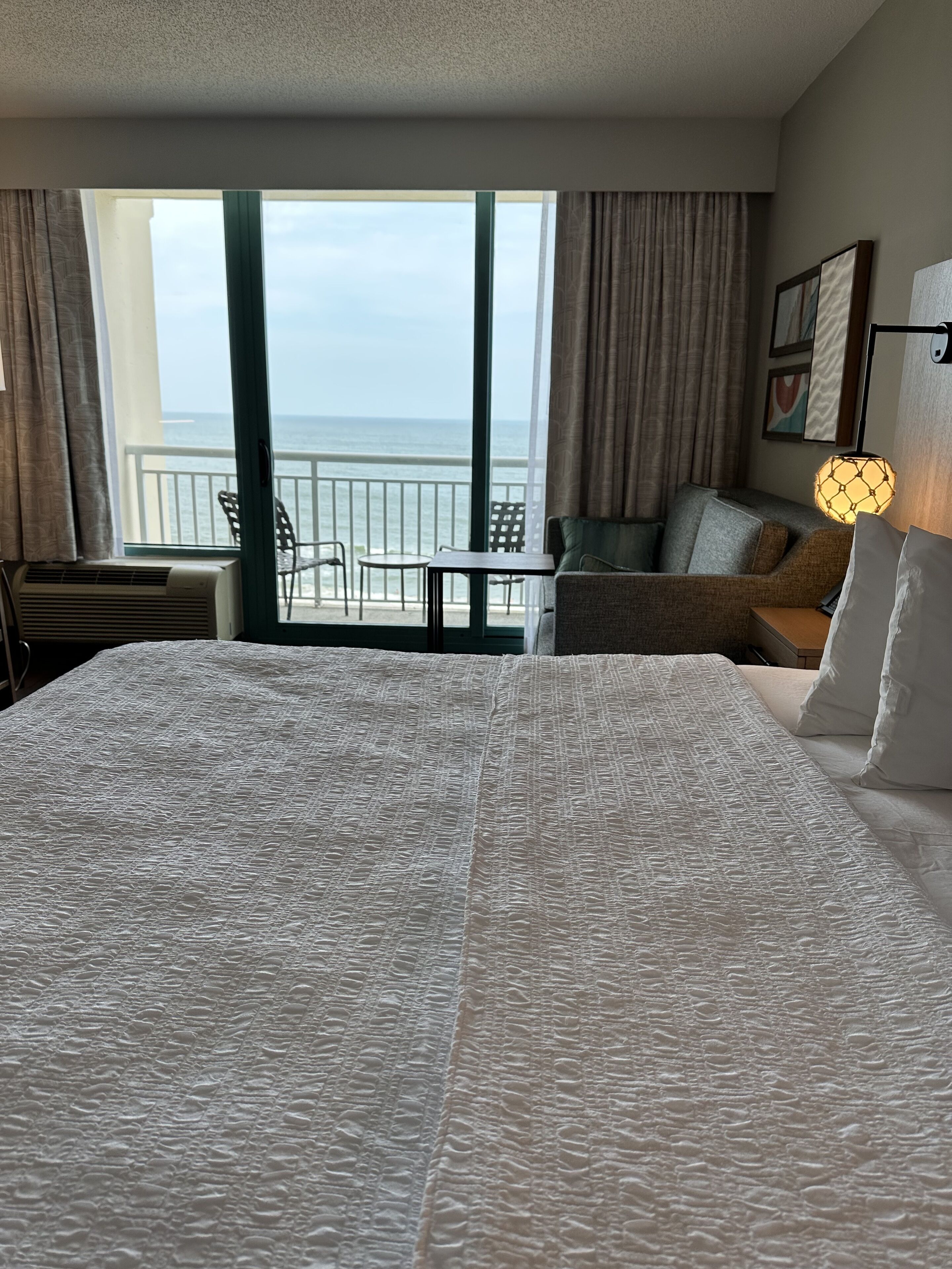 A hotel room with a large bed, a balcony with a view of the sea, and a seating area with a table and chairs.