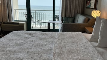 Una habitación de hotel con una cama grande, un balcón con vistas al mar y una zona de estar con una mesa y sillas.
