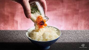 Une main verse un liquide transparent dans un bol de riz blanc.