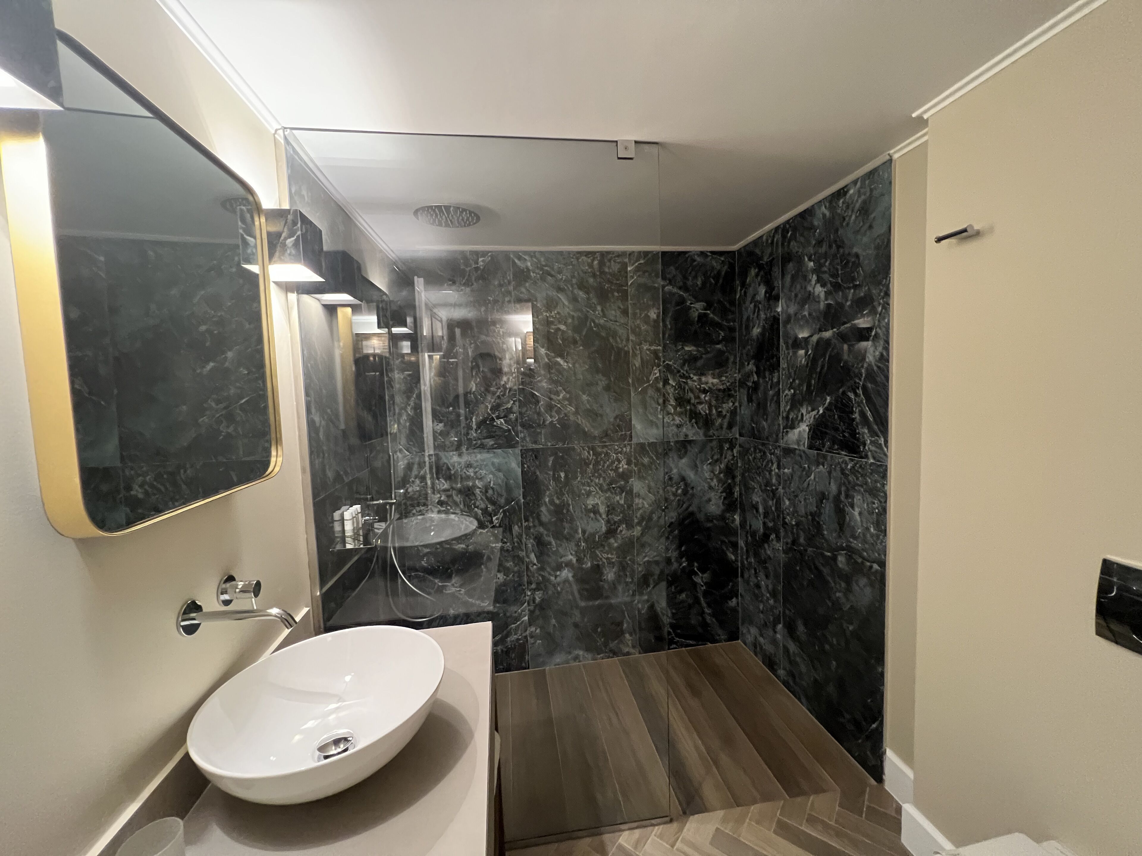 Un baño moderno con un espejo grande, un lavamanos blanco y una zona de ducha de mármol.