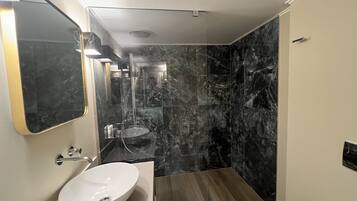 Un baño moderno con un espejo grande, un lavamanos blanco y una zona de ducha de mármol.