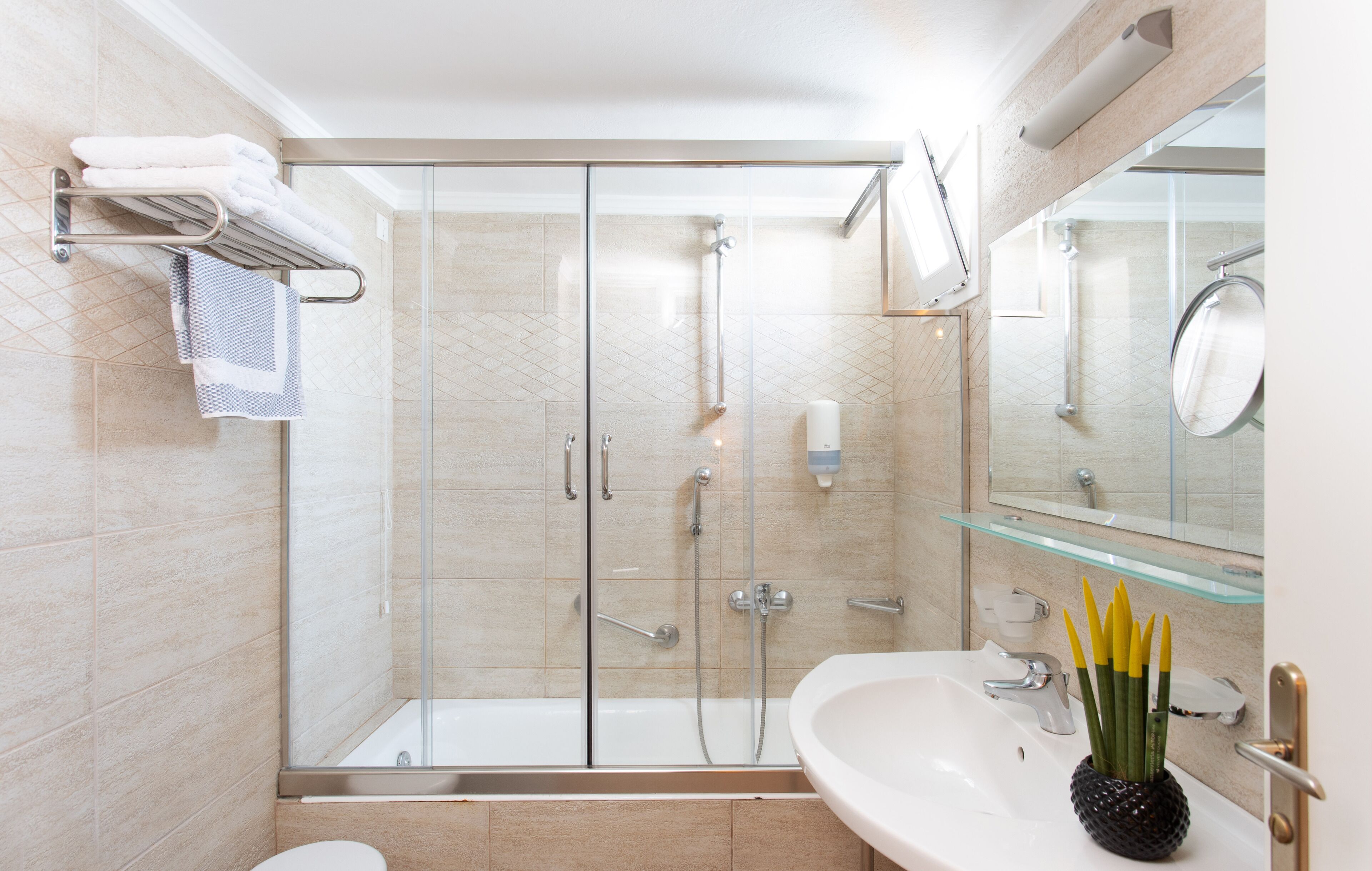 Une salle de bain moderne avec une douche à parois de verre, un lavabo blanc et un miroir surmonté d’une étagère en verre.