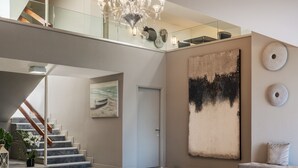 Um hall espaçoso com piso de mármore, escadaria, um banco e um grande quadro abstrato.