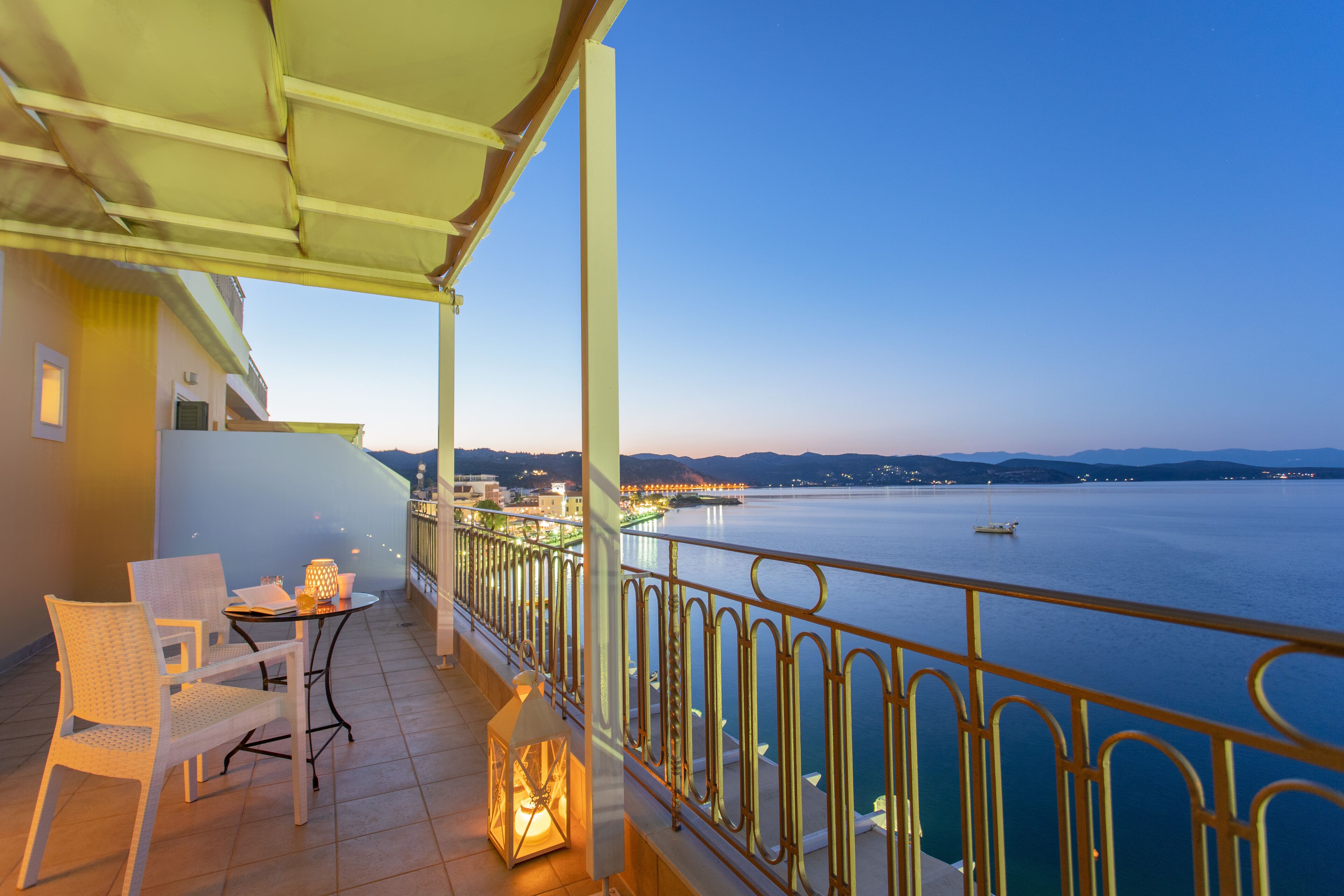 Een balkon met uitzicht op een rustig wateroppervlak, een hekwerk en een tafel met stoelen.