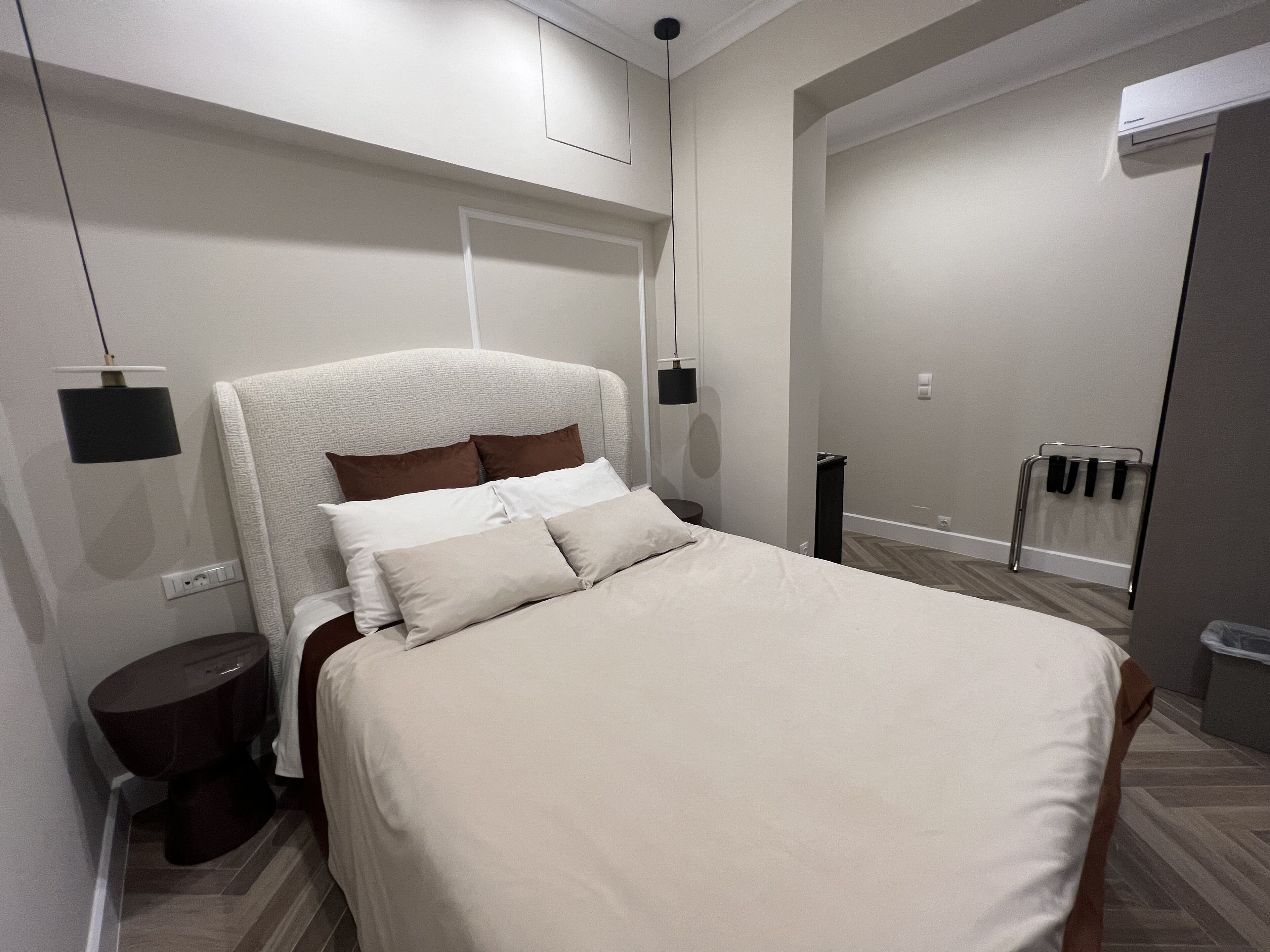 A modern bedroom with a large bed, a bedside table, a wall-mounted lamp, and a door leading to another room.