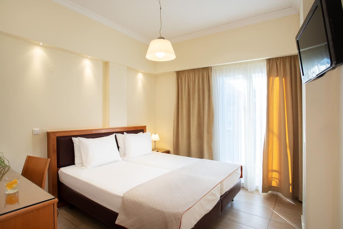 Habitació d'hotel amb un llit gran, una taula de nit, un televisor fixat a la paret i una finestra amb cortines.