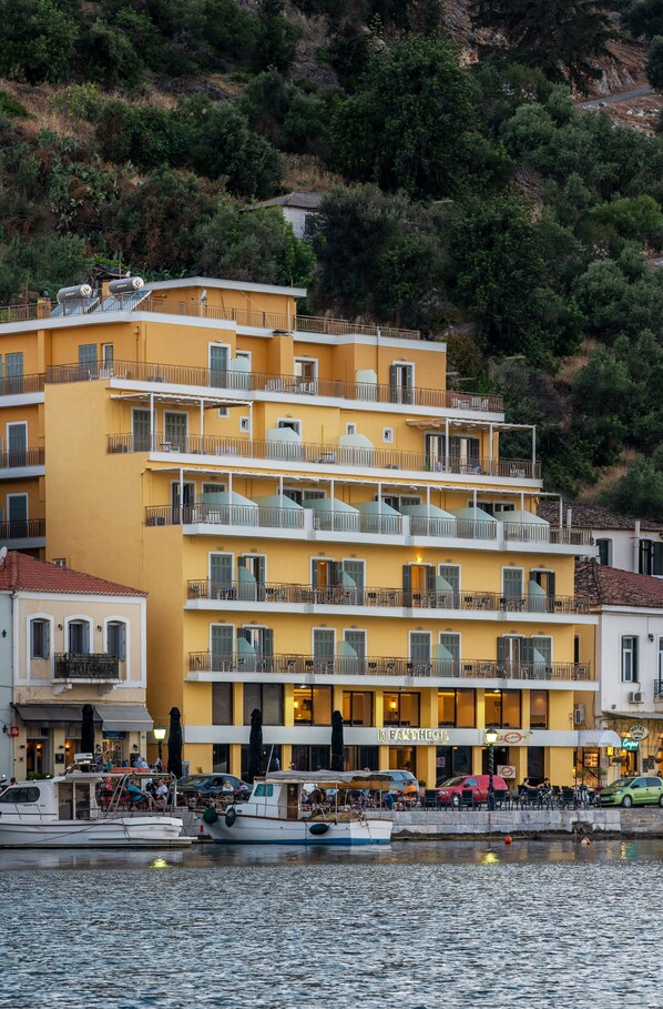 Un immeuble jaune à plusieurs étages, doté de balcons, avec un restaurant appelé « FANTHEON » au rez-de-chaussée, et des bateaux amarrés sur l’eau, devant le bâtiment.