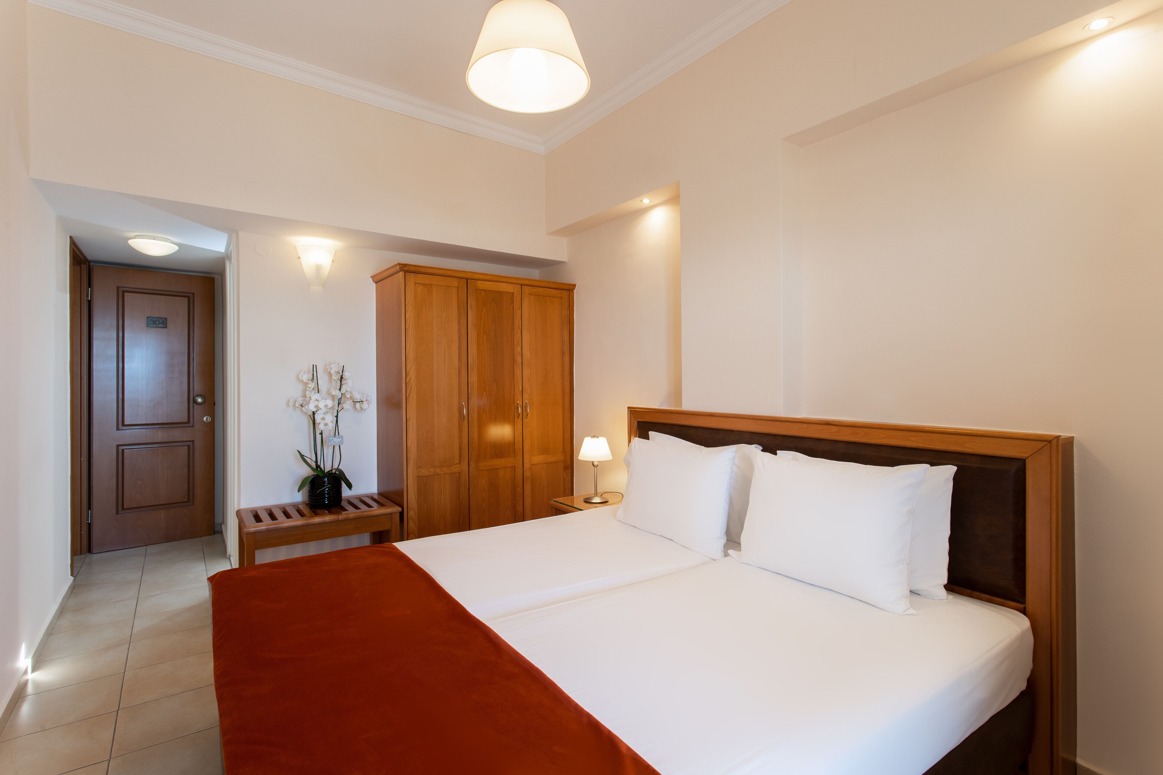 Una habitación de hotel con una cama grande, un armario de madera y un banco con un jarrón de flores.