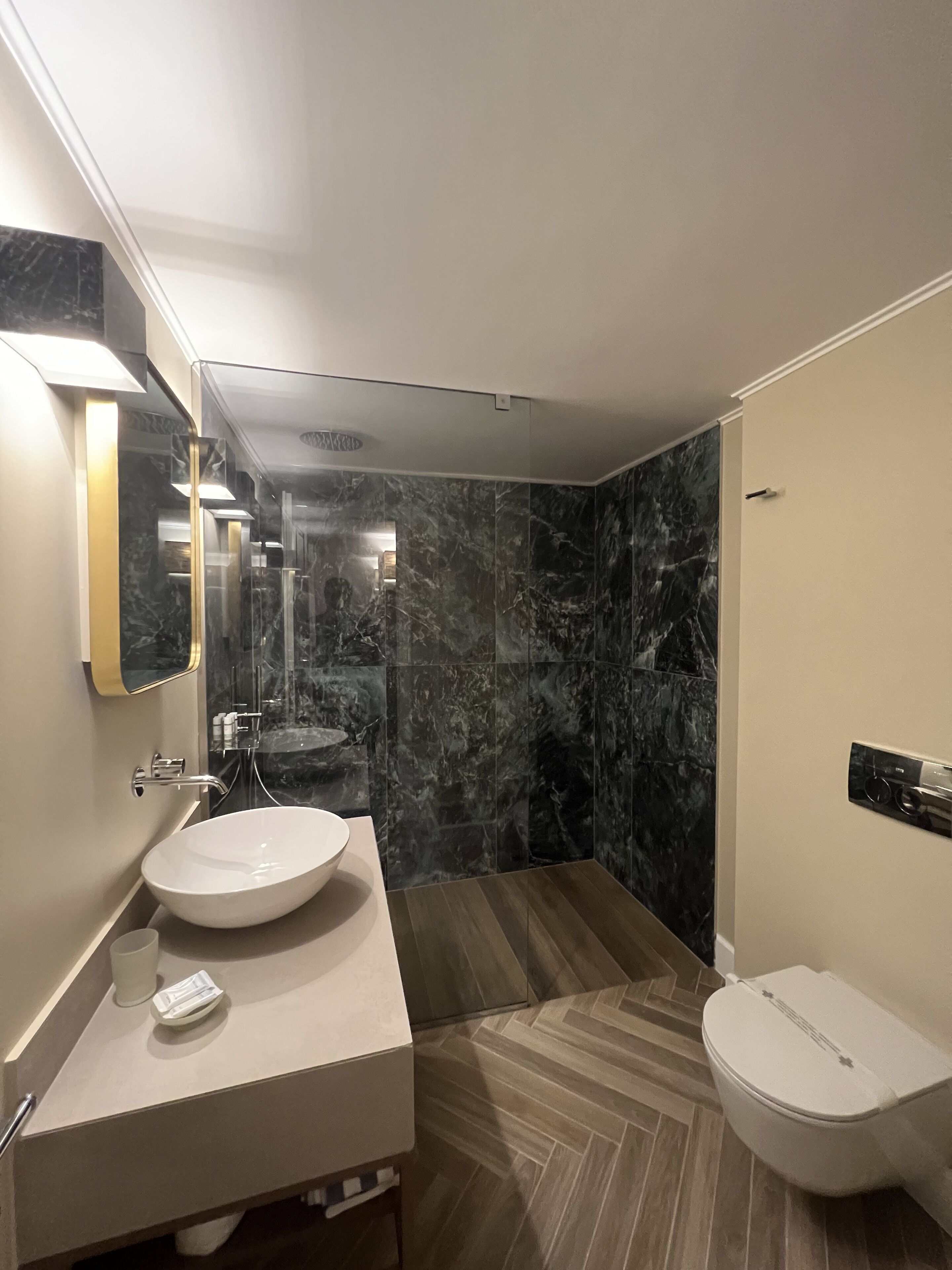A modern bathroom with a marble vanity, a sink, a toilet, and a shower area.