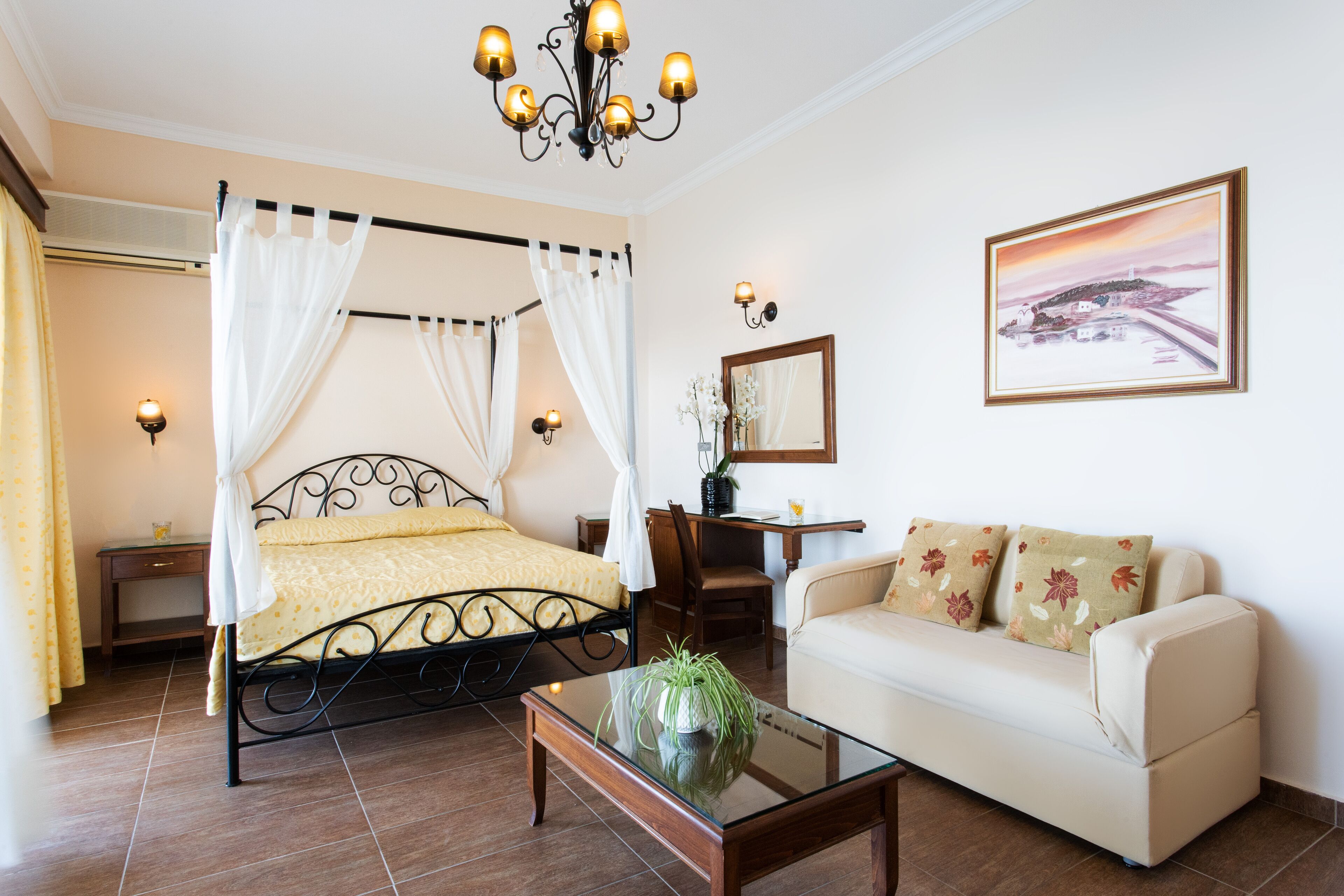 Une chambre à coucher avec un lit à baldaquin, un canapé, une table basse en verre et un tableau accroché au mur.