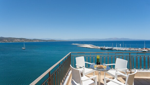 Varanda com mobiliário de vime branco com vista para uma marina com barcos e mar azul cristalino.