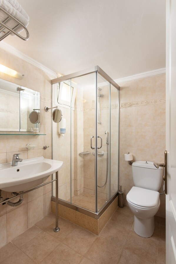 Un baño con ducha de mampara de vidrio, un lavabo, un inodoro y un espejo.