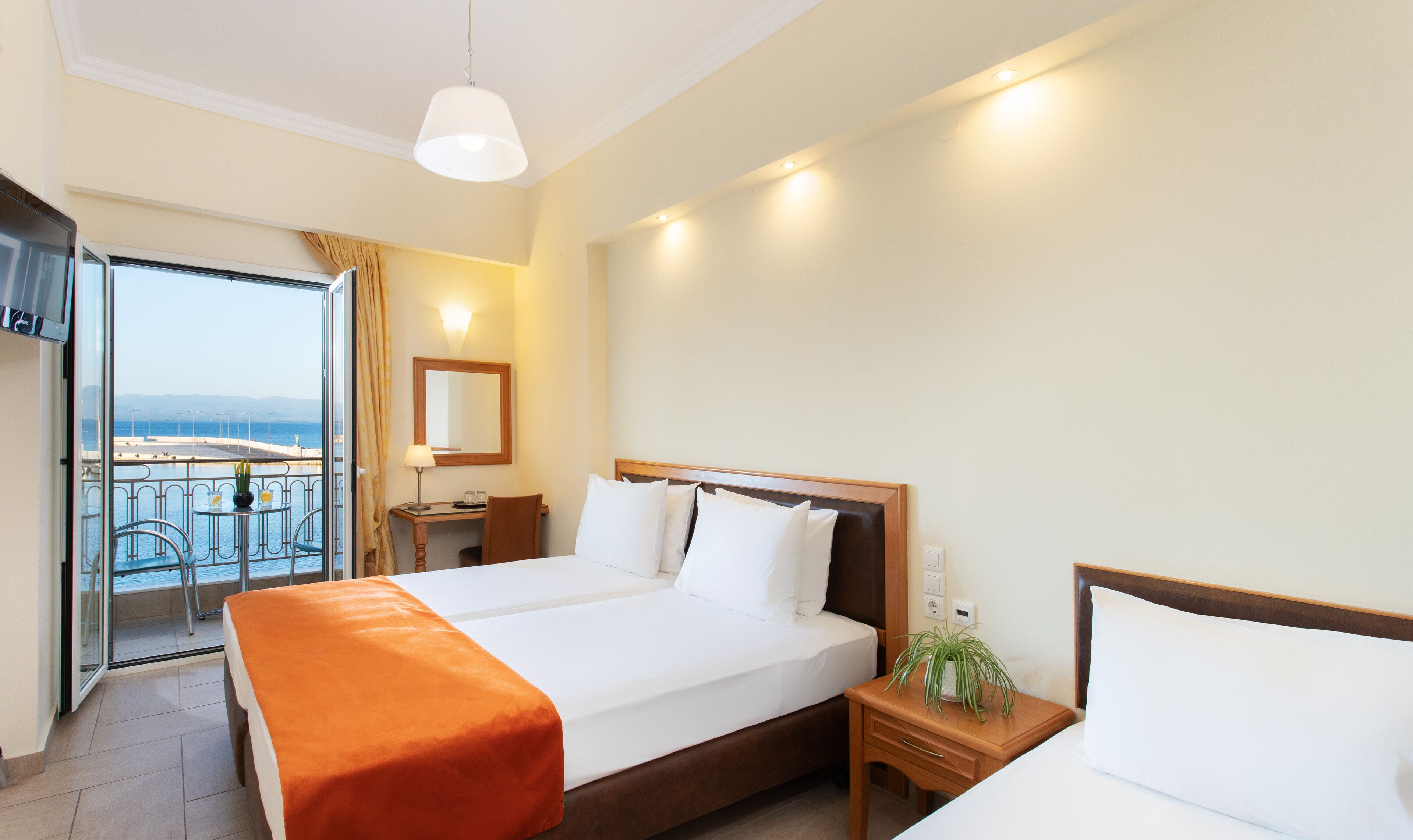 Un cuarto de hotel con cama, escritorio, silla, mesita de noche, espejo y vista al mar.