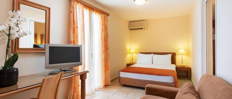 Habitación de hotel con cama, escritorio con computadora, televisor, sofá y planta en maceta.