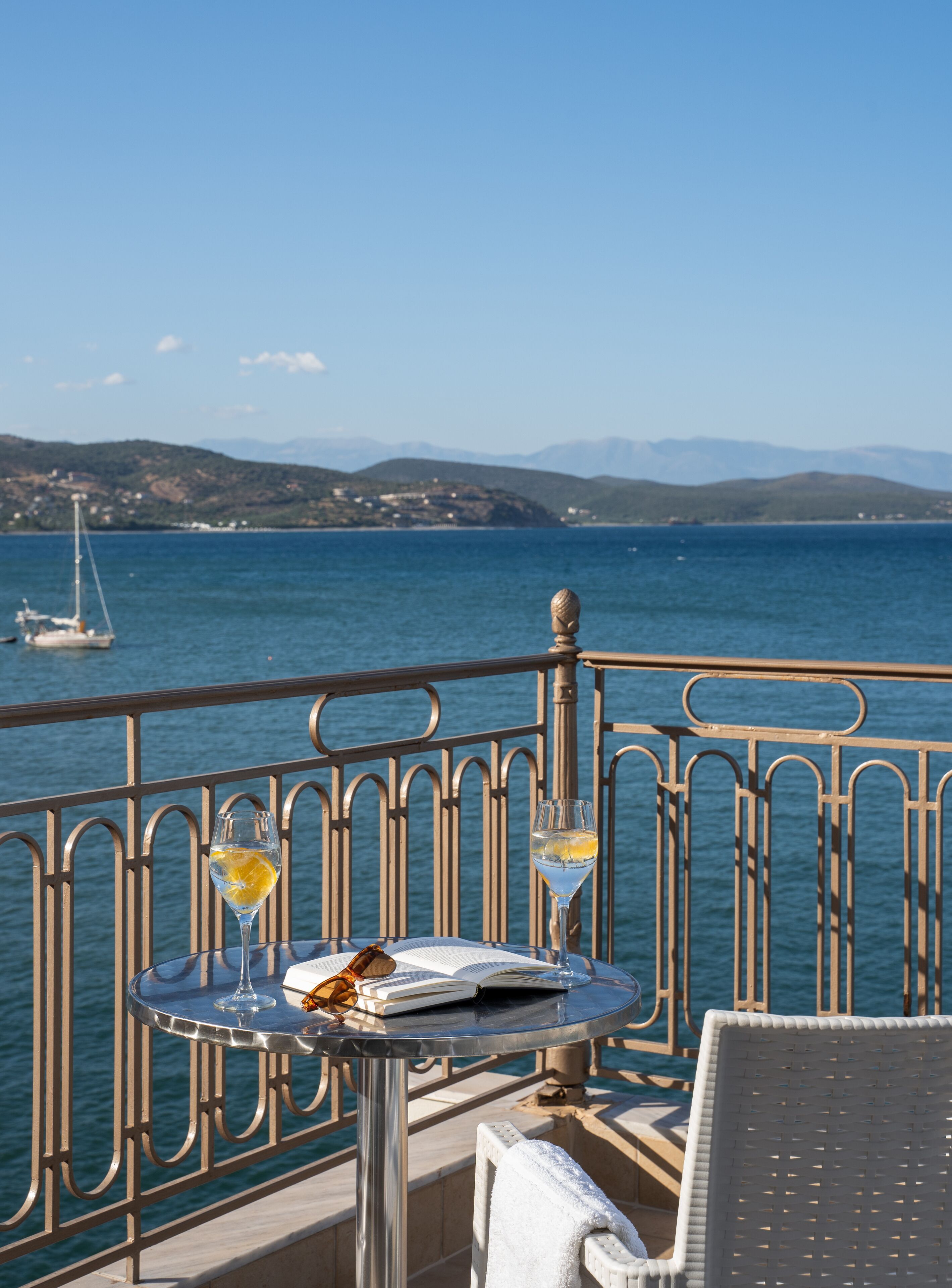 A balcony with a table, two glasses of white wine, and an open book.