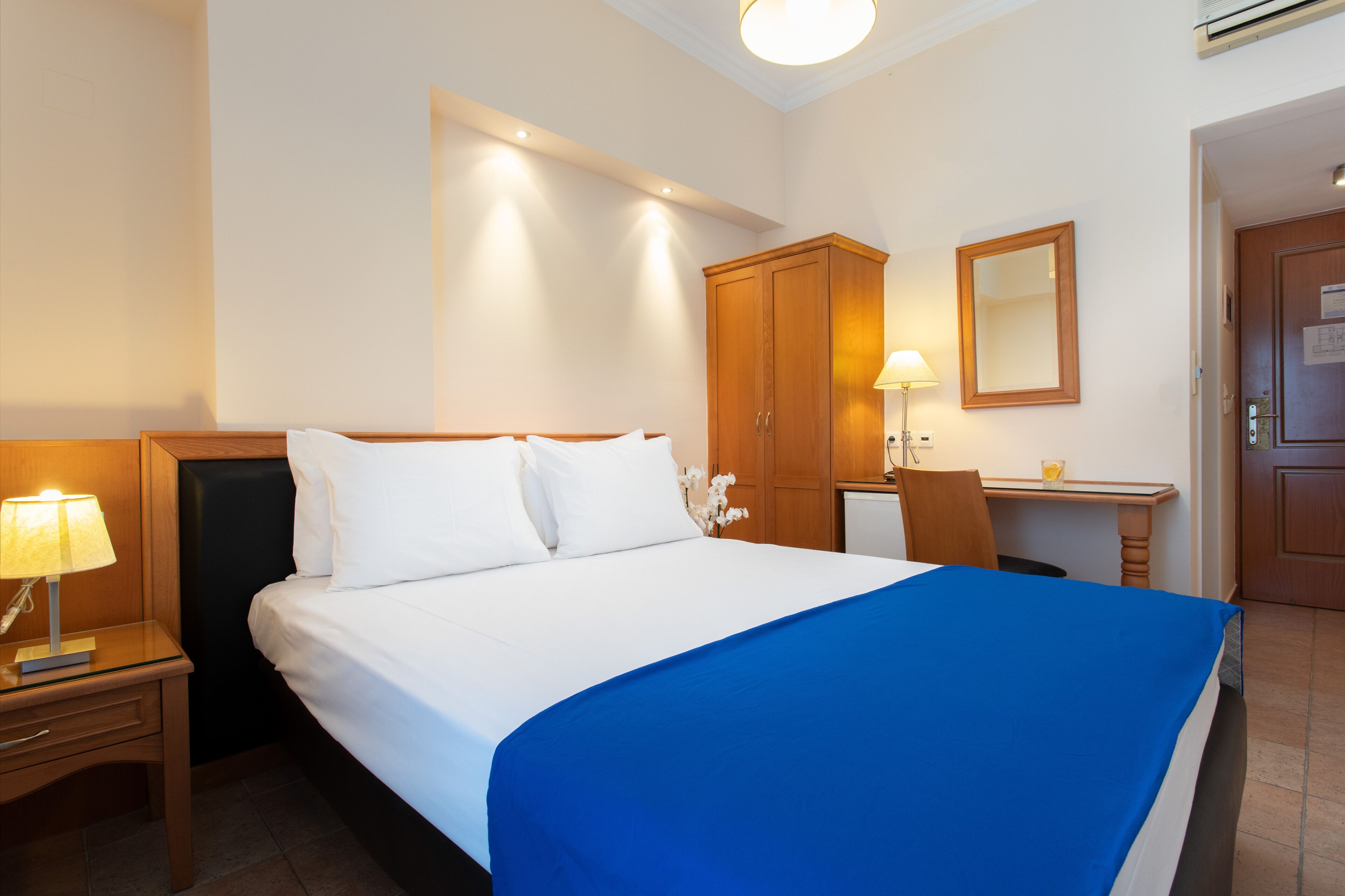 A hotel room with a bed, bedside table, lamp, desk, chair, and wardrobe.