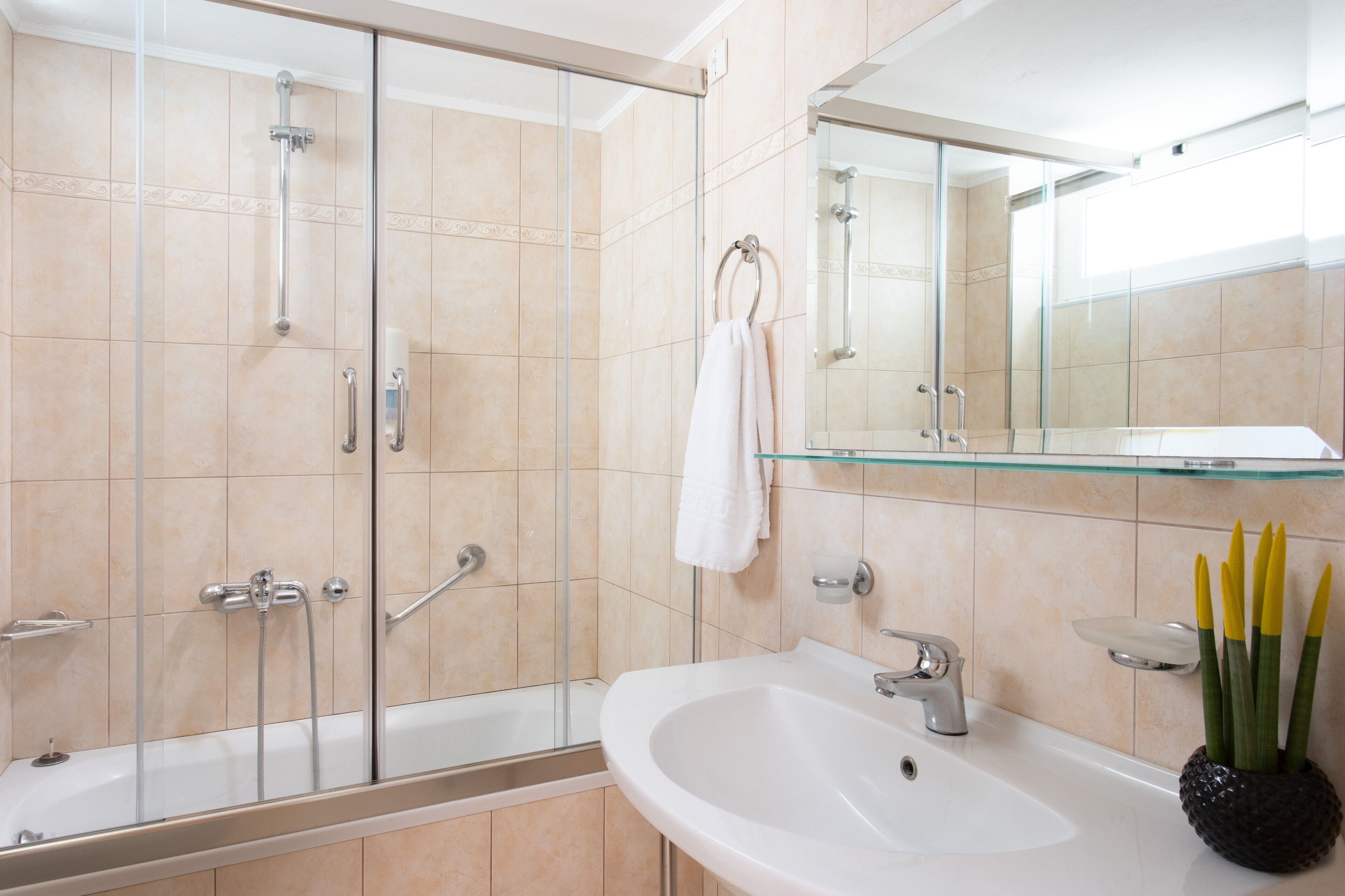 A modern bathroom with a glass-enclosed shower, a white sink, and a glass shelf.