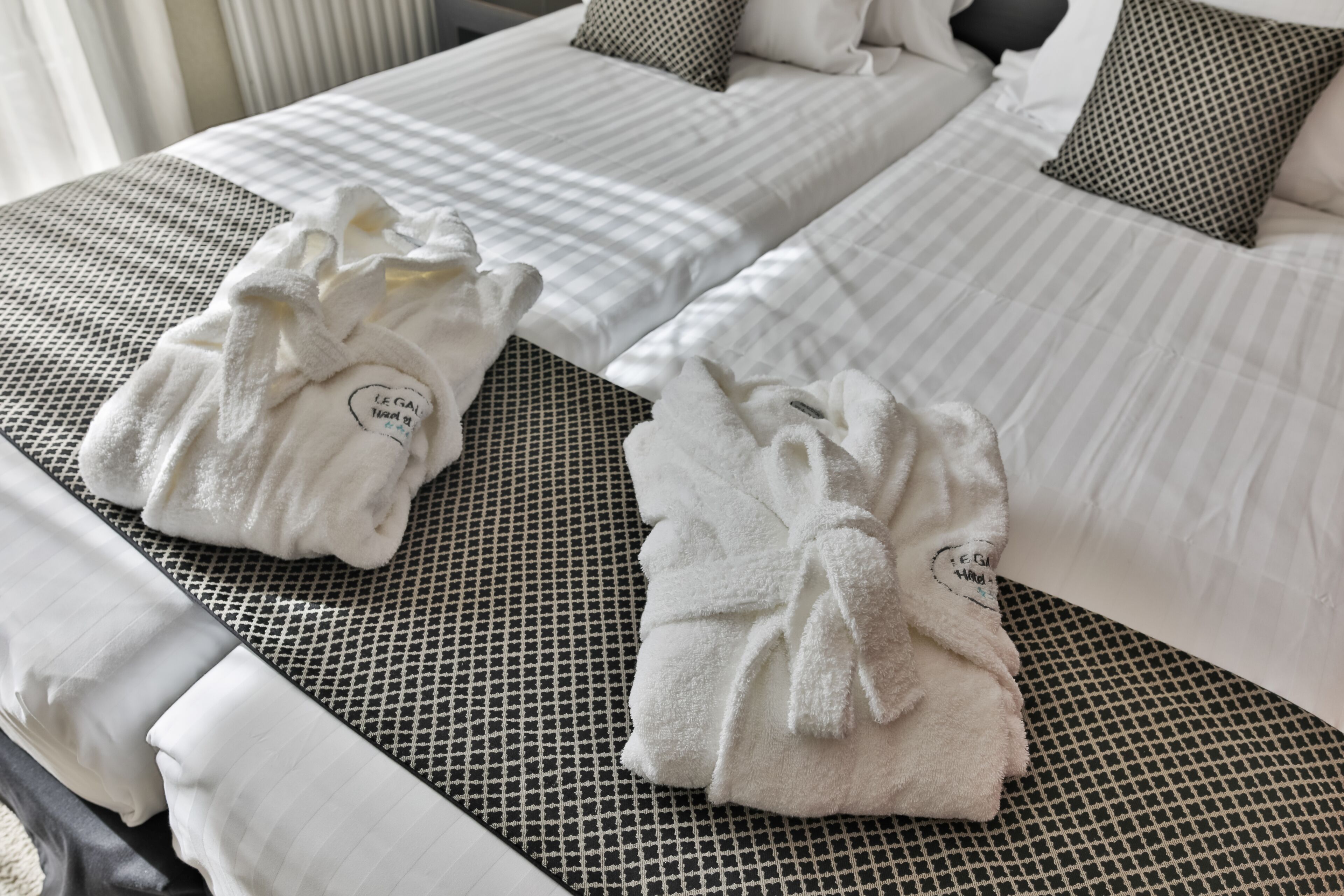 A hotel room with two beds, each with a neatly folded white towel and a pillow with a black and white pattern.