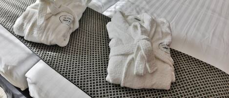 Habitación de hotel con dos camas, cada una con una toalla blanca doblada y un cojín con estampado blanco y negro.