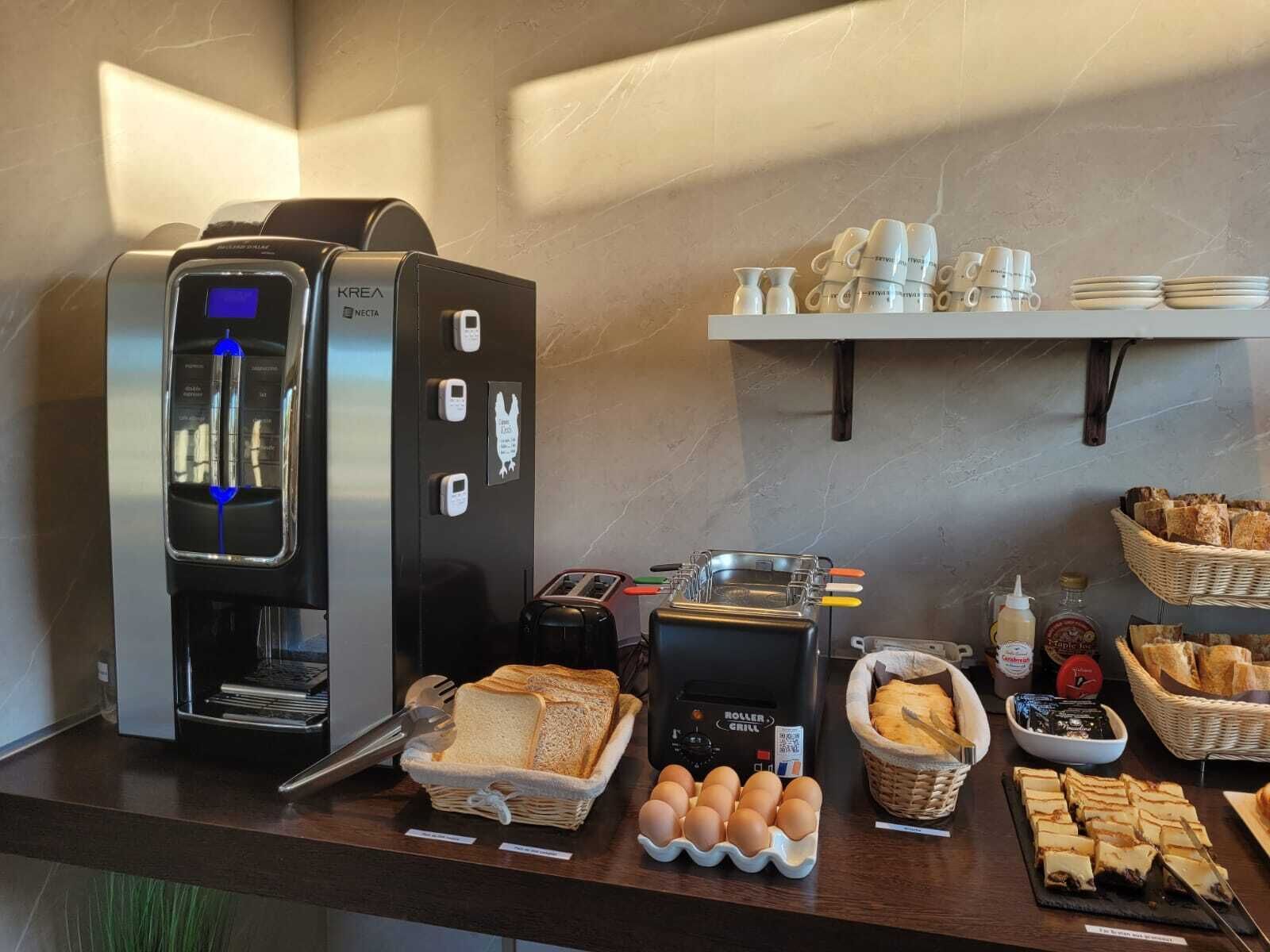 Um buffet de café da manhã com máquina de café, torradeira, ovos, pão e diversas geleias e patês.