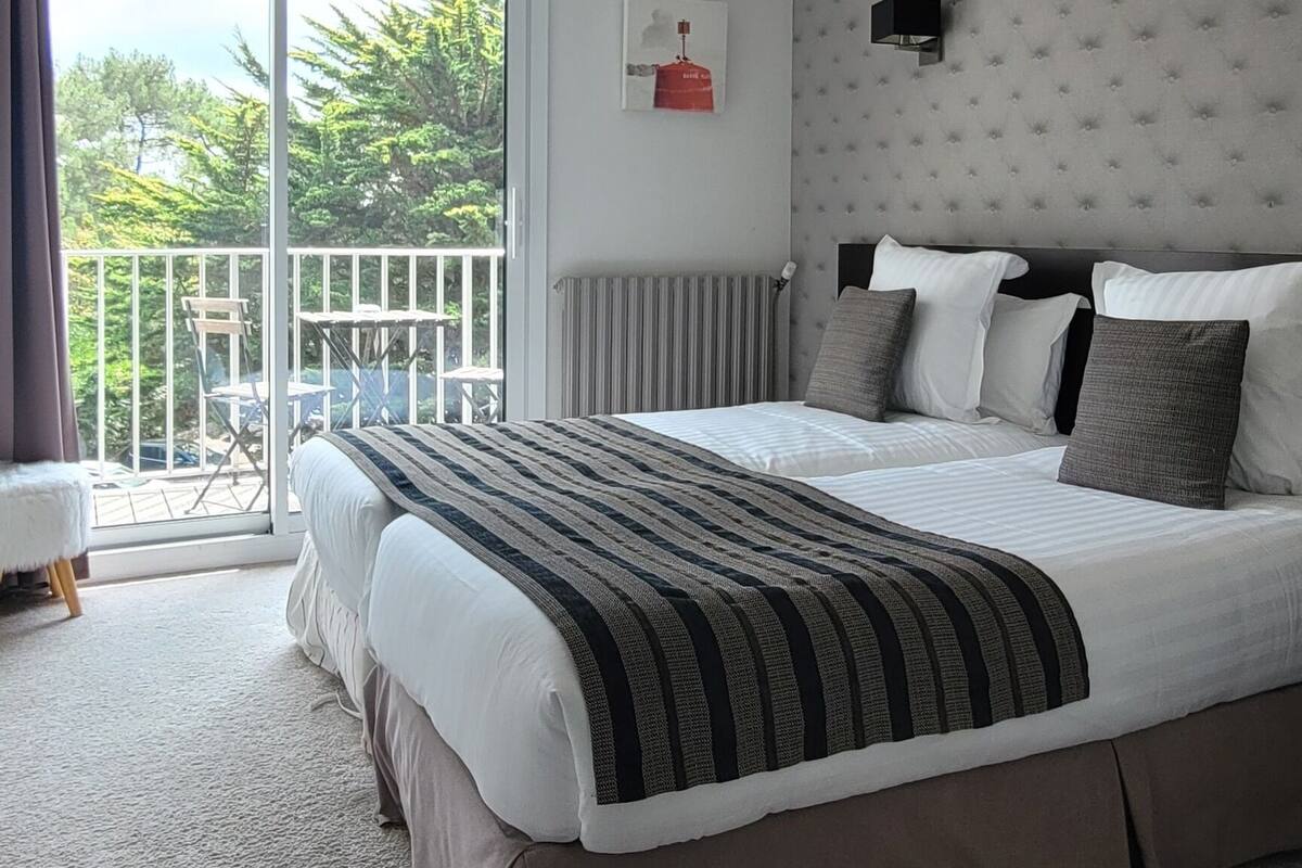 A bedroom with a large bed, a balcony with a table and chairs, and a hanging light fixture.