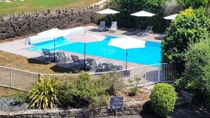 Una piscina con sillas de descanso y sombrillas, rodeada de follaje y un muro de piedra.