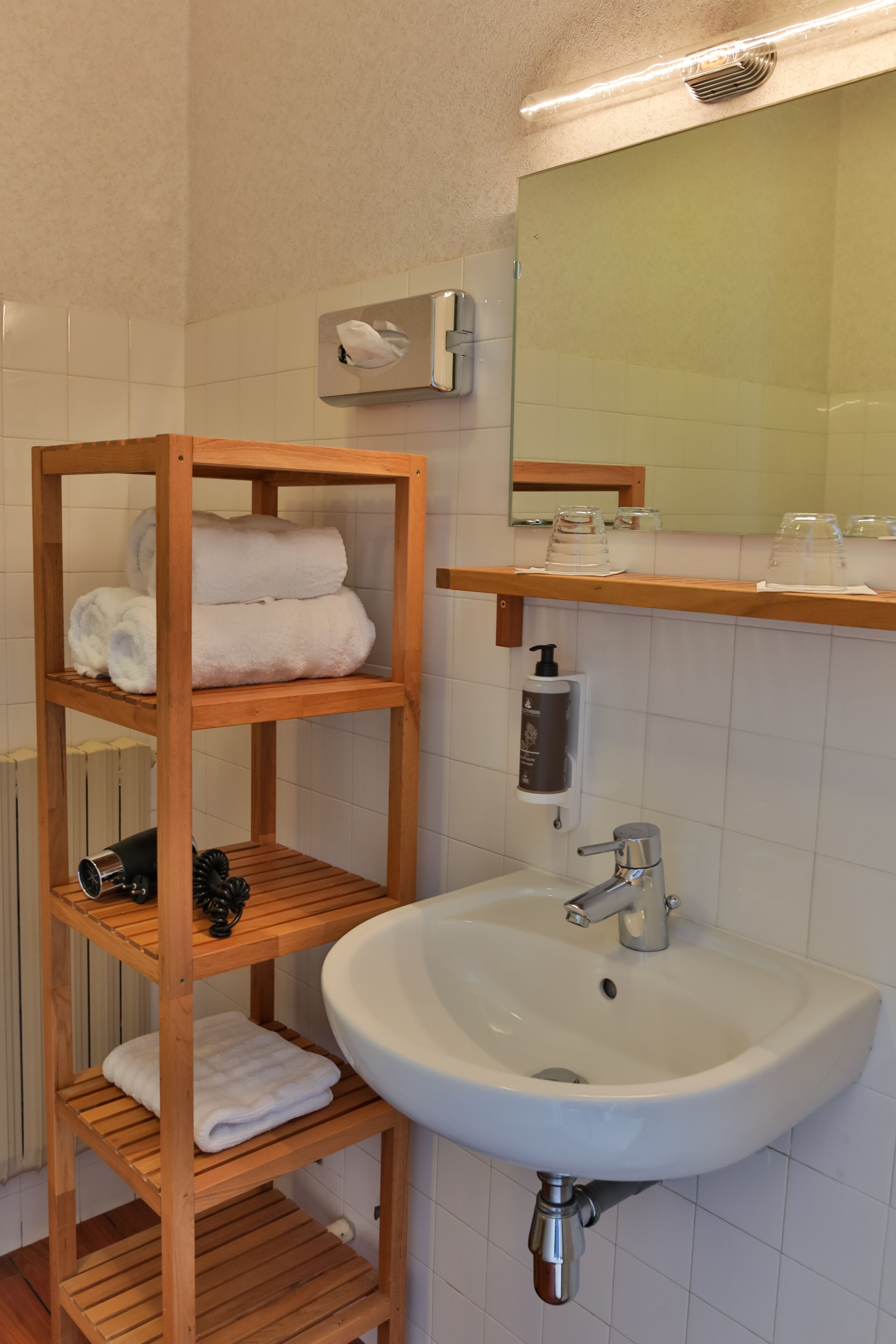 Une salle de bain avec une étagère en bois où sont posées des serviettes, un lavabo et un miroir au-dessus.