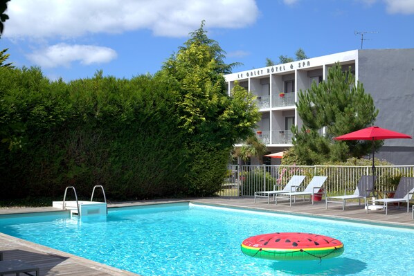 A swimming pool with a wooden deck, lounge chairs, and a red umbrella. - Le Galet Hôtel & Spa (Saint-Philibert)