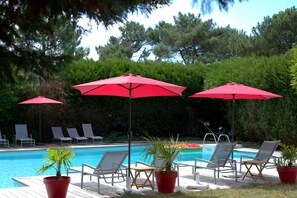 A poolside area with lounge chairs and red umbrellas. - Le Galet Hôtel & Spa (Saint-Philibert)
