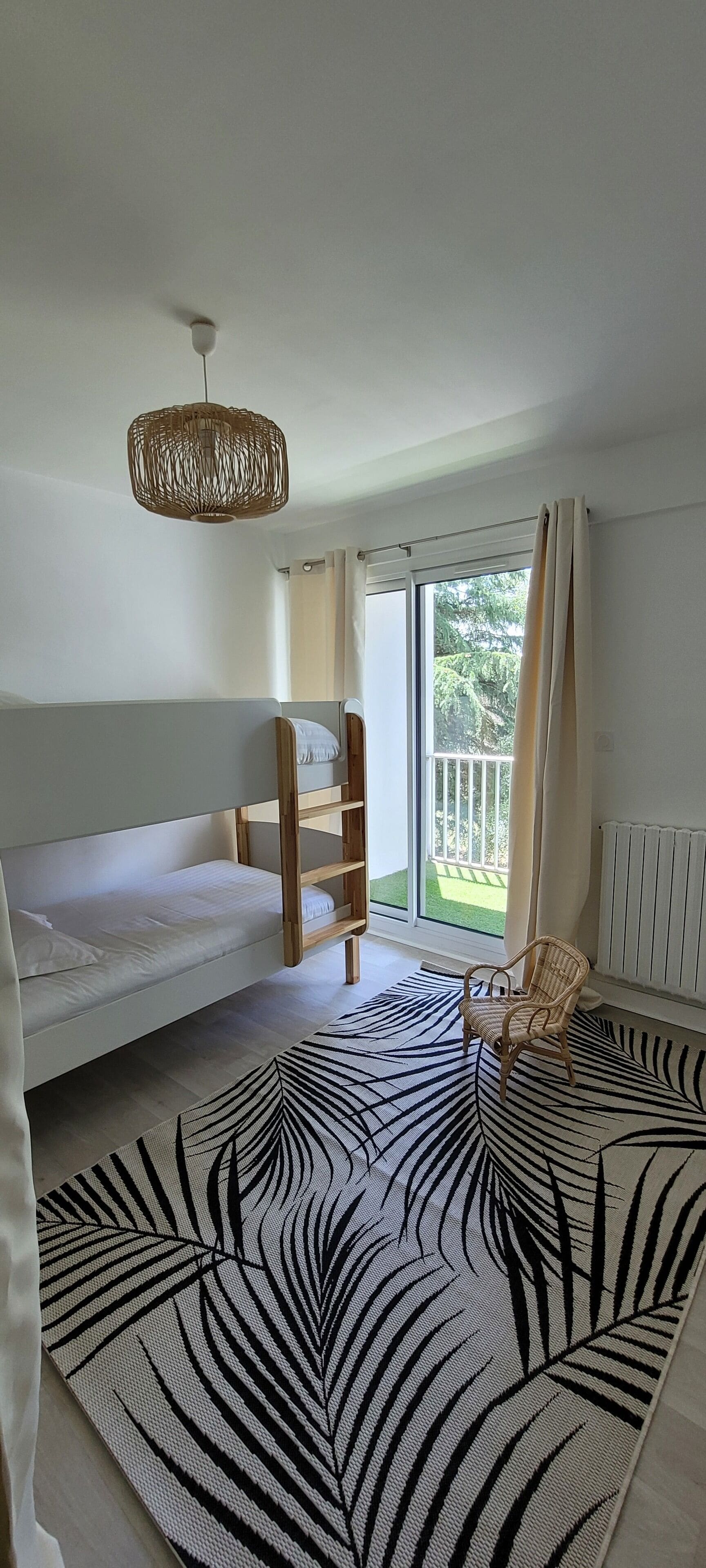 A room with a bunk bed, a wicker ceiling light, a view of a garden through a sliding door, and a zebra-patterned rug.