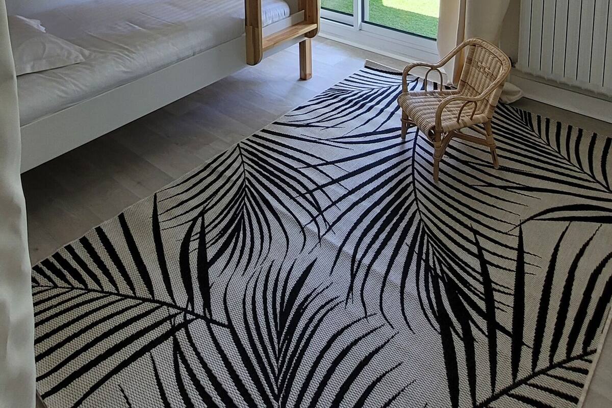 A room with a bunk bed, a wicker ceiling light, a view of a garden through a sliding door, and a zebra-patterned rug.