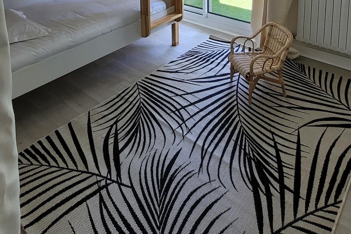 A room with a bunk bed, a wicker ceiling light, a view of a garden through a sliding door, and a zebra-patterned rug.