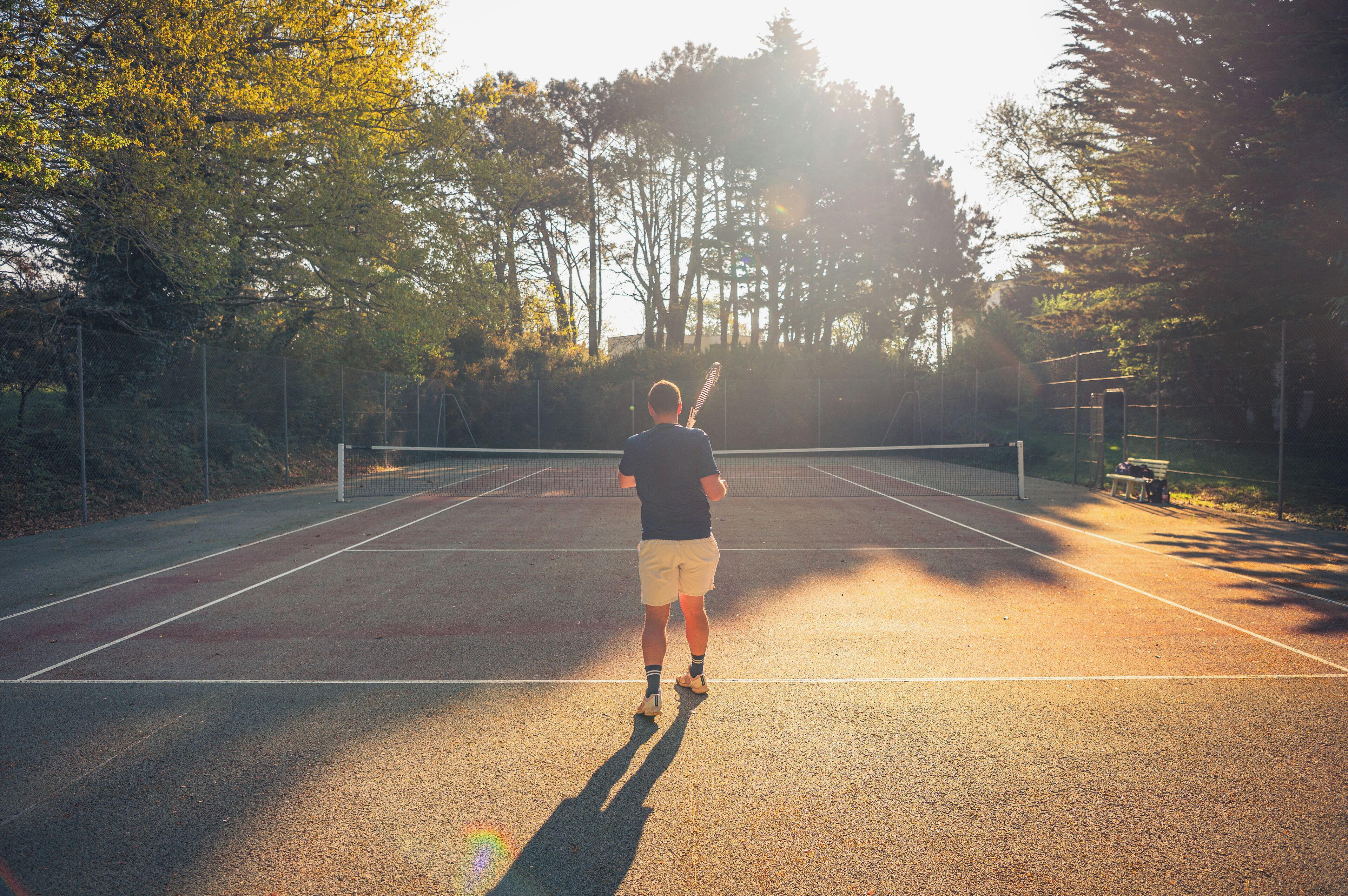 Una cancha de tenis con una red, rodeada de árboles y una valla.
