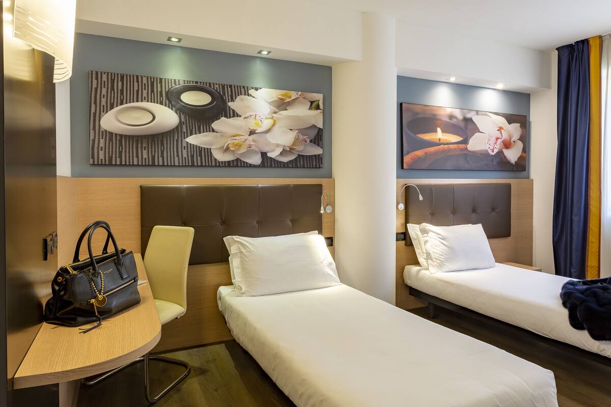 A hotel room with two single beds, a small desk, and a chair.