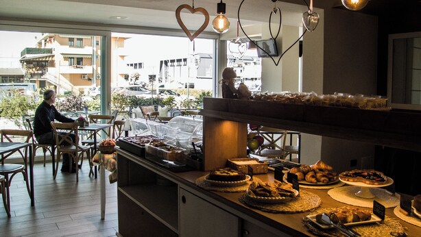 Un café où l’on peut admirer une variété de viennoiseries exposées sur le comptoir, et où une personne est assise à une table.