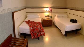 Une chambre d’hôtel avec deux lits, une table de chevet en bois, une chaise et une lampe fixée au mur.