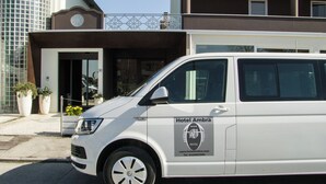 Un fourgon blanc arborant le logo « Hôtel Ambra » est garé devant un immeuble.