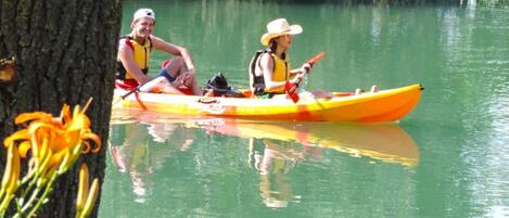 Two people kayaking on a calm river surrounded by trees.