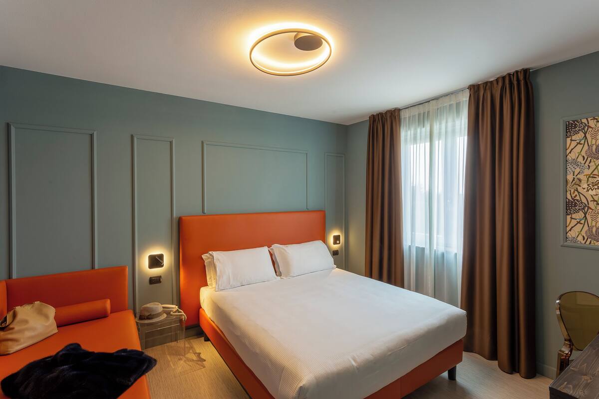A hotel room with a large bed, a nightstand, a chair, and a window with curtains.