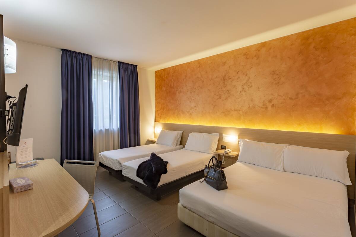 A hotel room with two beds, a desk, a chair, a lamp, and a wall with a textured pattern.