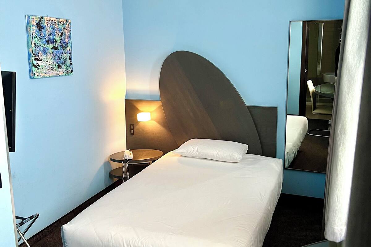 A hotel room with a bed, bedside table, lamp, and a mirror.