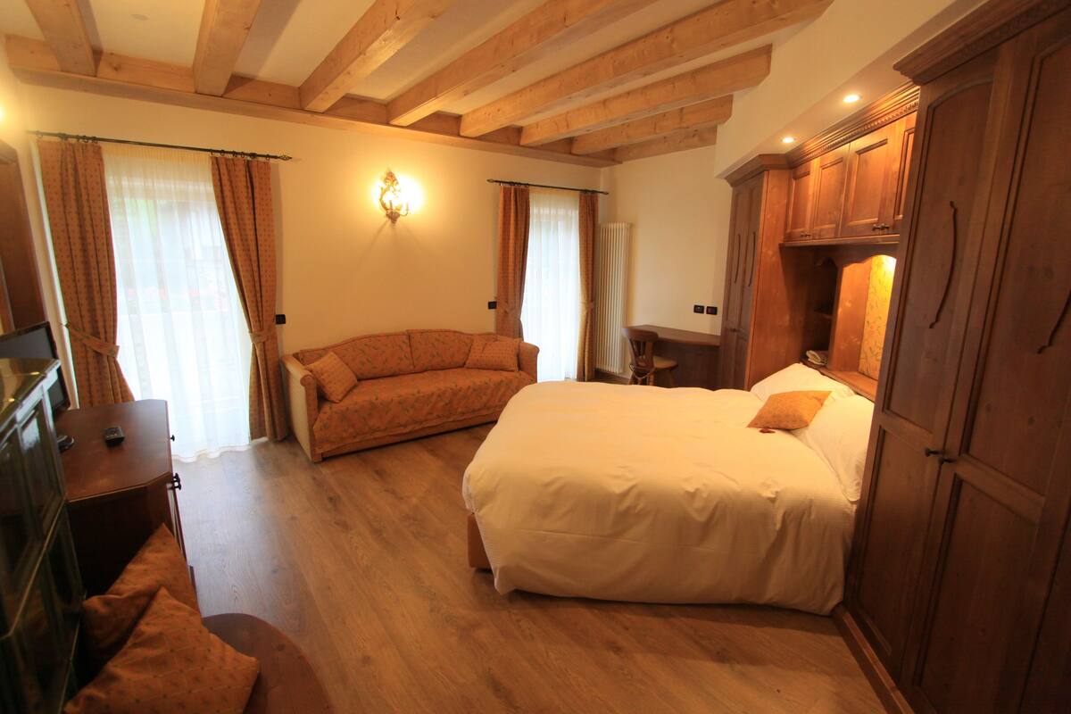Een slaapkamer met een groot bed, een bank, houten balken in het plafond en een kledingkast.