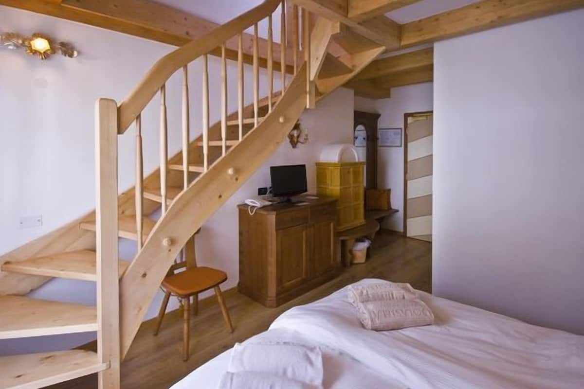 Een slaapkamer met een houten trap, een bed, een bureau en een stoel.