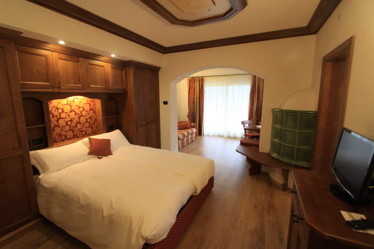 Een hotelkamer met een groot bed, houten kasten, een televisie en uitzicht op de gang.
