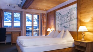 A hotel room with a large bed, wooden headboard, a desk, and a chair. - Hotel Tenne (Saas-Fee)