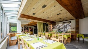 A restaurant with multiple tables set for dining, a wooden ceiling, and large windows allowing natural light. - Hotel Tenne (Saas-Fee)